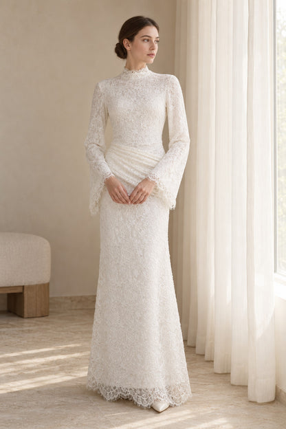 Lilia white lace dress on a model beside a window, showing the high neckline, long sleeves and ruched hip panel