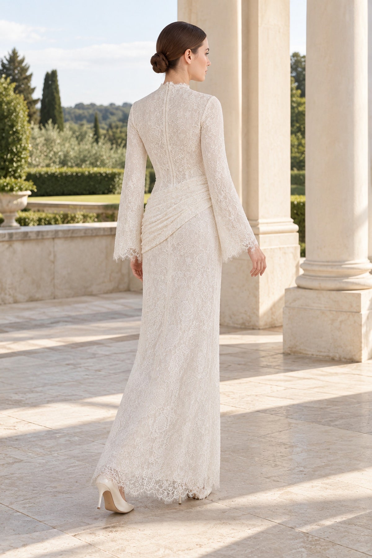 Rear three-quarter view of the Lilia white lace dress outdoors, showing long sleeves and diagonal hip ruching