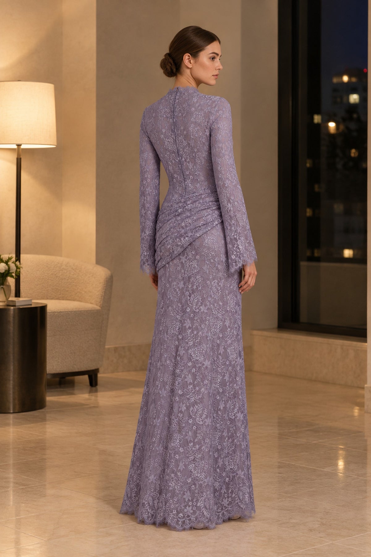 Rear three-quarter view of the Lilia lilac lace maxi dress in a warm interior, showing long sleeves and back draping.