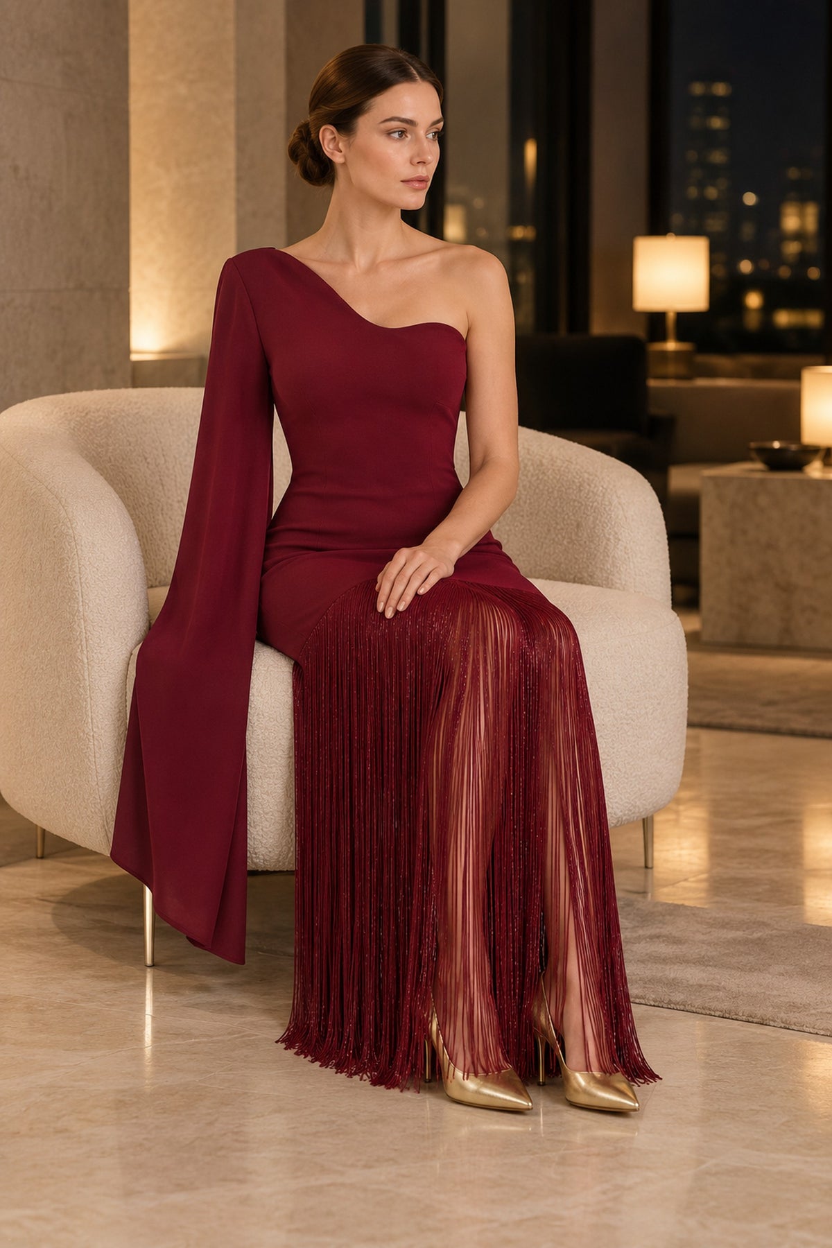 APERLAMIRI Seraphine burgundy one-shoulder cape-sleeve fringe maxi dress — seated indoor evening setting