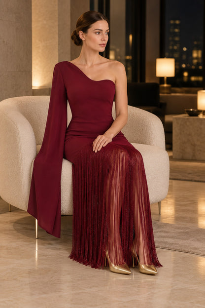 APERLAMIRI Seraphine burgundy one-shoulder cape-sleeve fringe maxi dress — seated indoor evening setting